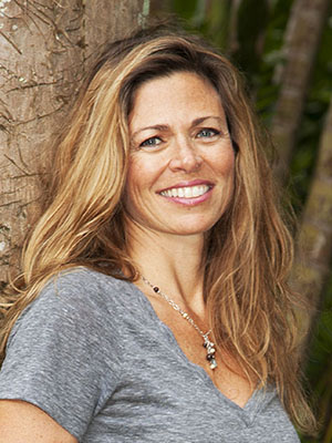 Maui artist, Christine Waara, standing in front of a palm tree at her studio